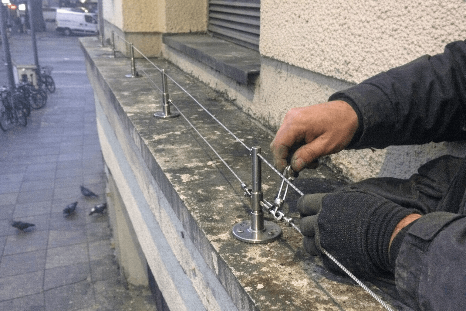 Techniker spannt ein Edelstahlseil mit Spannschloss vor einer Klinkerfassade